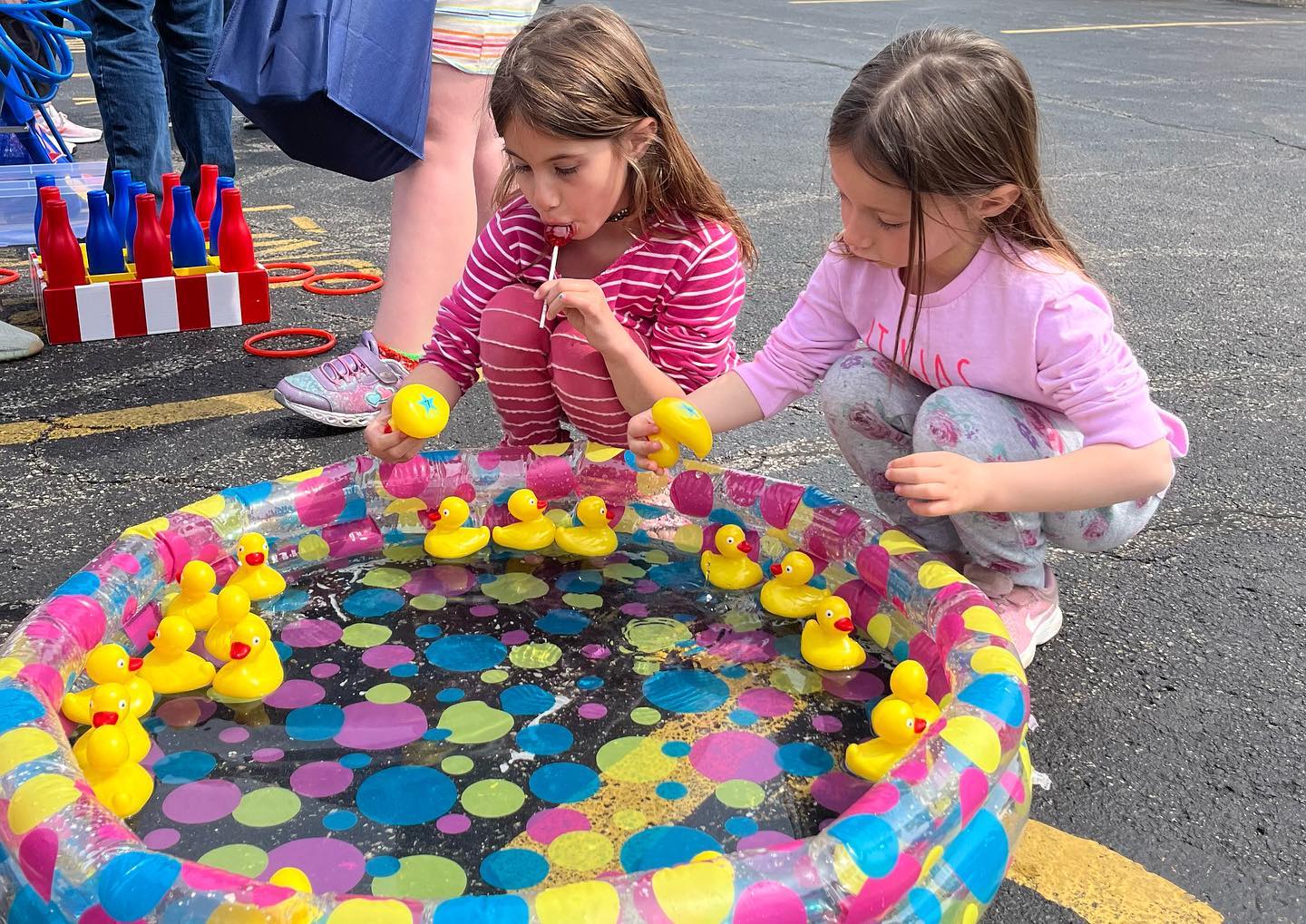 Two little girls picking up rubber ducks out of a kiddie pool